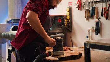 Craftsperson works with orbital sander with sandpaper on lumber to achieve smooth finish, checking quality. Woodworking expert in carpentry shop using angle grinder to fix wooden surface, camera A photo