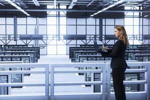 Engineer in data center checking rigs and infrastructure, doing maintenance. IT expert planning and executing high tech server hub facility migrations and upgrades using laptop photo