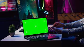 Green screen laptop next to man playing with friends online, shooting asteroids together in spaceship flying game. Mockup notebook and gamer cooperating with teammates in coop videogame photo