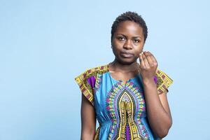 Portrait of african american model trying to explain something on camera, gesticulating and explaining a thing over blue background. Young confident woman in ethnic attire talking to someone. photo