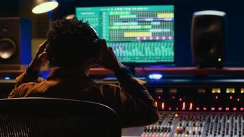 Sound designer editing tracks by adjusting volume levels with panel board knobs and sliders, studio control room. Audio technician mixing and mastering hit song with digital software. Camera A. photo