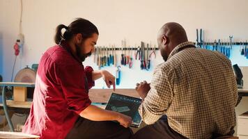 BIPOC artisan and apprentice comparing wood art piece schematic with CAD software 3D render on laptop. Woodworking experts in studio crosscheck drawing on clipboard with notebook blueprint, camera A photo