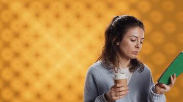 Woman reading book, turning page and holding disposable cup of coffee, isolated over studio background. Bookworm enjoying novel and caffeinated drink early in the morning, camera A photo