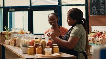 Vendor giving fresh homemade sauces to customer, recommending ethically sourced additives free goods. African american client examining organic natural products at local store. photo