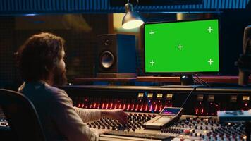Audio specialist uses greenscreen workstation to watch tutorials and understand how to blend recorded tunes. Professional expert in tracking sounds, controls knobs and levers. Camera A. photo