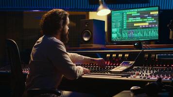 Audio technician mixes individual tunes to create balanced sound after recording session in professional studio. Sound engineer editing tracks with mixing console and production software. Camera A. photo