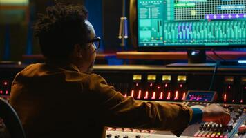 African american producer working at mixing panel in recording studio. Using control desk and digital audio workstation software on pc to edit and process tracks, post production concept. Camera A. photo