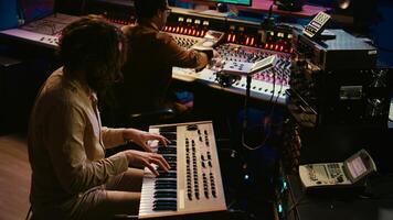 Skilled artist singer recording songs on electronic midi controller, singing on piano and creating tracks with audio engineer. Young musician composer editing music on console. Camera B. photo