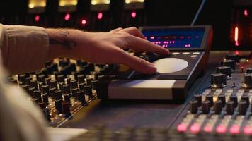 Audio technician uses mixing console and faders in control room, remote control for adjusting sound on mixer. Music producer changes volume level, creates tracks with technical equipment. Camera A. photo