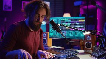 Music producer playing his song on piano keyboard and singing at microphone, recording soundtrack to edit on mixing console. Composer working with synthesizer in home studio. Camera B. photo