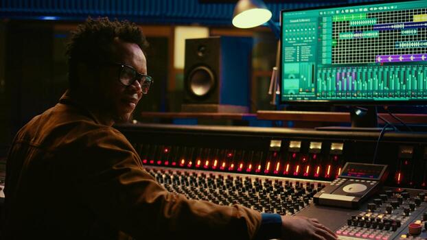 retrato de africano americano audio técnico usos mezcla consola con perillas y deslizadores en controlar habitación, edición grabaciones y agregando sonido efectos experto música productor a mezclador. cámara b. foto