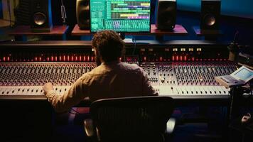 Sound designer mixing and mastering tracks on audio console in control room, using daw software on computer and editing files. Technician creating new music in professional studio. Camera B. photo