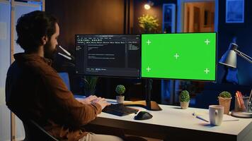 Programmer typing complex code on green screen computer in neon lit home office, developing software application. Teleworking IT specialist doing remote project tasks on mockup PC monitor, camera B photo