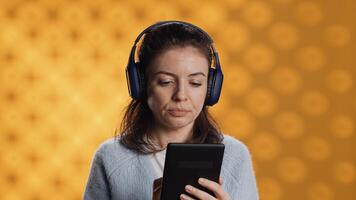 Woman wearing headphones, practicing new language vocabulary using online app on tablet, isolated over studio background. Lady speaking foreign phrases, reading them on device screen photo