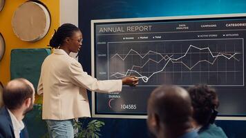 Marketing assistant presenting infographics in a status update meeting, studying data to establish key performance indicators. African american employee operating interactive board. Camera A. photo