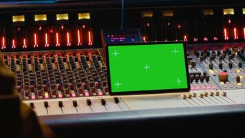 Music producer holding a tablet with greenscreen display on mixing console in control room, twisting knobs and pushing faders to edit audio recordings. Processing sounds. Camera A. photo