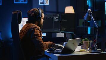 Engineer typing code in apartment office, using javascript programming language to develop software application. It admin using multimonitor desktop setup and notebook to finish tasks, camera A photo