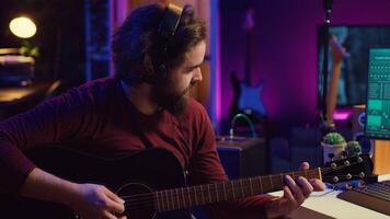 Sound engineer playing acoustic guitar and using mixing console to record music, adjusting volume and adding sound effects to tunes. Artist works with digital audio workstation software. Camera A. photo