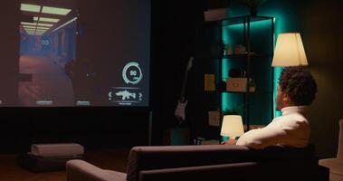Man sitting on couch, playing first person shooter videogame on smart TV with gun shooting laser bullets. Gamer arriving home, ready to start game with dark atmospheric industrial setting photo