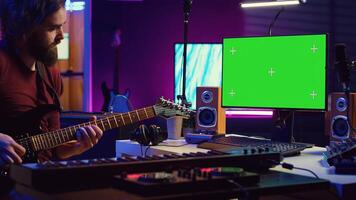 Male singer learning to play a new song on acoustic guitar, using greenscreen on computer to watch online tutorials. Artist songwriter practicing with his instrument in home studio. Camera A. photo