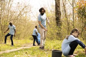Young activist using rake to clean up dead leaves from the woods, preserving the natural ecosystem and planting trees. Man doing voluntary work for a conservation project, raking ground. photo