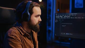 Computer scientist listening music while writing lines of code during remote job shift in home office. IT specialist enjoying audio podcast, coding on desktop PC, camera B close up photo