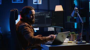 Software programmer putting headphones on while developing code, making time pass faster during remote job shift. IT professional doing multitasking in apartment office while listening music, camera A photo