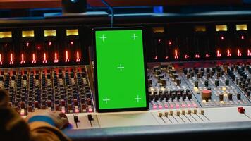 Audio expert processing sounds next to tablet with isolated mockup, working in post production with mixing console and technical gear. Producer pushing switchers and sliders. Camera A. photo