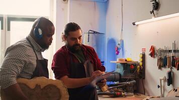 Craftsperson and colleague look over technical schematics to make commissioned wooden object. Manufacturer and coworker analyze blueprints to execute furniture assembling woodworking project, camera B photo