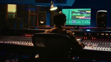 African american sound producer editing tracks on audio software and console, adjusting volume levels and adding effects in post production. Technician producing new hit song in studio. Camera B. photo