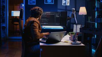 Software programmer putting headphones on while developing code, making time pass faster during remote job shift. IT professional doing multitasking in apartment office while listening music, camera B photo