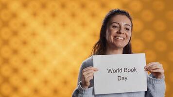 Smiling book club member holding placard with world book day message, isolated over studio background. Radiant bookworm recording promoting literacy importance, camera A photo