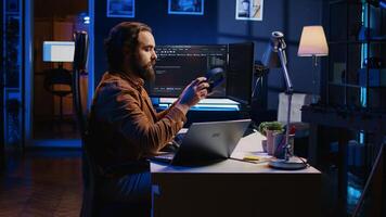 Developer writing lines of code on multimonitor PC setup during remote job shift. IT expert doing multitasking in neon lit home office, listening music, drinking coffee, camera B photo
