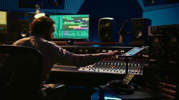 Sound engineer counting down for artist in vocal booth to start singing and producing new music, control room technical gear. Skilled audio technician operating knobs and sliders. Camera B. photo