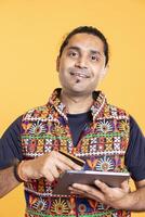 Portrait of jolly man looking at debit card to read banking account, feeling happy to do online purchases, studio background. Cheerful man does internet shopping using digital tablet, having fun photo