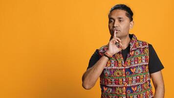 Annoyed indian man doing shushing hand gesturing, irritated by noise, having negative mood. Person placing finger on lips, doing quiet sign gesture, studio background, camera A photo
