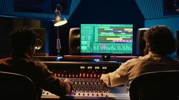 Team of artist and technician editing audio after recording session in control room, mixing and mastering tracks on console in control room. Pressing buttons and pushing sliders. Camera B. photo