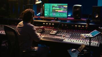 Audio technician mixes individual tunes to create balanced sound after recording session in professional studio. Sound engineer editing tracks with mixing console and production software. Camera A. photo