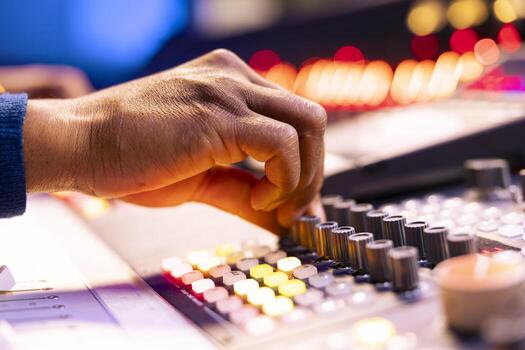 African american sound engineer operates audio console in control room, pushing faders and twisting knobs to adjust settings on tracks. Music producer composing new music in studio. Close up. photo