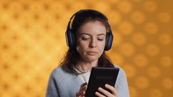 Woman wearing headphones, practicing new language using internet app on digital tablet, isolated over studio background. Person repeating foreign words, reading them on device photo