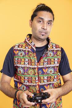 Gamer annoyed after losing online multiplayer videogame, being defeated by rival players. Indian man gutted after seeing game over message, holding controller, studio background photo