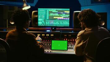 Artist and sound designer examine digital editing software and mockup on tablet, collaborating on composing a hit for new album. Musician working with audio technician in studio. Camera B. photo