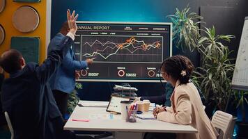 Diverse colleagues reviewing monthly sales infographics on interactive board, measuring feedback on previous initiatives for future improvements. Management team in a meeting. Camera B. photo