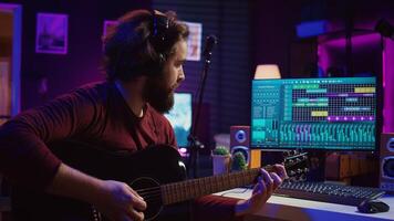 Sound engineer playing acoustic guitar and using mixing console to record music, adjusting volume and adding sound effects to tunes. Artist works with digital audio workstation software. Camera B. photo