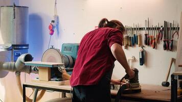 Carpenter making modifications on blueprint drawings, using angle grinder on wood. Man using orbital sander gear after consulting schematics, assisted by african american apprentice, camera A photo