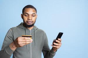 Happy excited african american man making a purchase online with credit card, entering banking credentials to pay for something on promotion. Confident young guy shopping on internet. photo