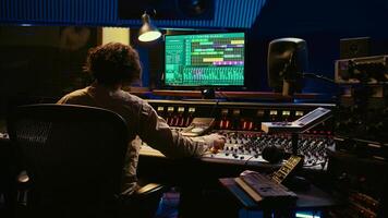 Music producer editing tracks with mixing console and audio software in studio, pressing key buttons and twisting knobs in control room. Sound engineer producing tunes and adjusting volume. Camera B. photo