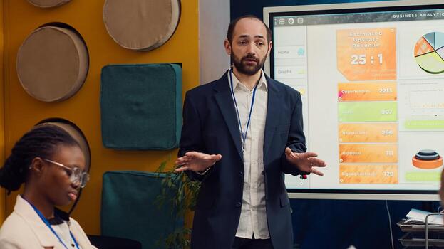 Management consultant gathering his employees for a status update meeting in boardroom, interactive presentation with the latest data. Success metrics and key performance indicators. Camera A. photo