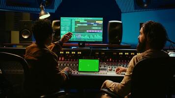Professional engineer and musician mixing tracks next to isolated display on tablet, editing audio after recording session to produce a hit song. Artist collaborates with sound designer. Camera B. photo