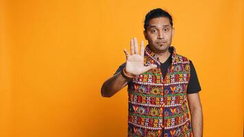 Stern indian man doing stop hand gesture sign, complaining. Authoritative person doing firm halt sign gesturing, wishing to end concept, isolated over studio background, camera B photo